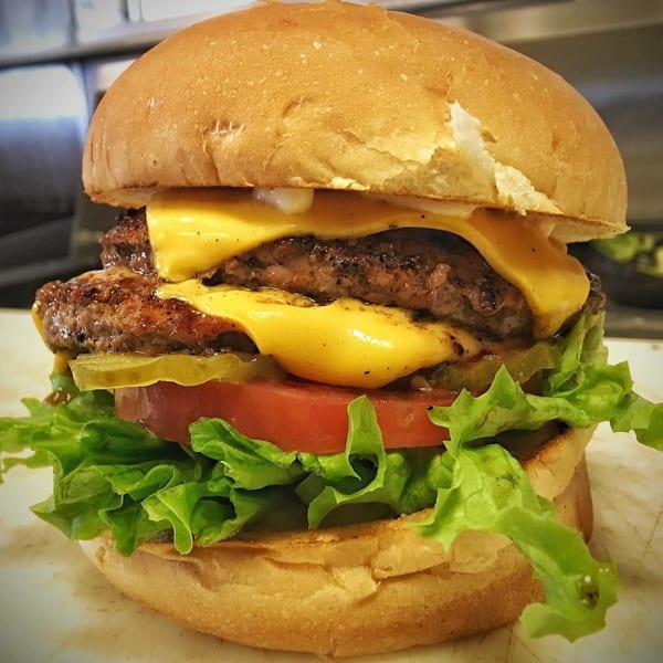 A Bubba's Texas Burger Shack double cheeseburger with lettuce, tomato, and pickles on a bun.