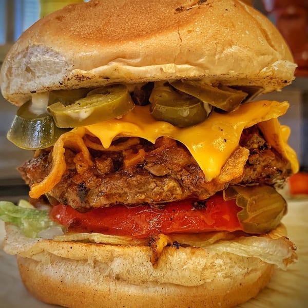 A close-up of a Bubba's Texas Burger Shack burger with melted cheese, jalapeños, and onion rings.