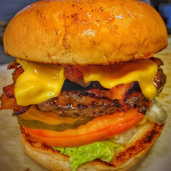 A close-up of a Bubba's Texas Burger Shack burger with melted cheese, bacon, tomato, and lettuce.