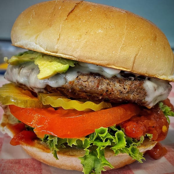 A Bubba's Texas Burger Shack burger with melted cheese, avocado, pickles, tomato, and lettuce.
