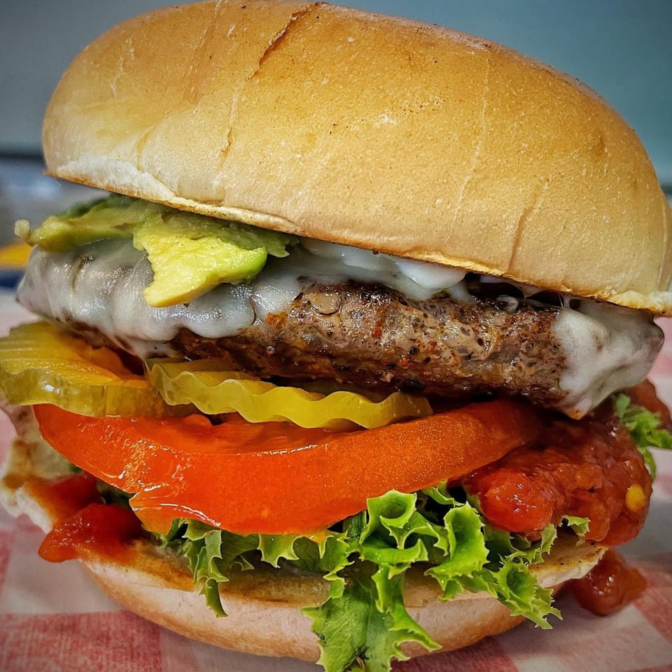 A Bubba's Texas Burger Shack burger with melted cheese, avocado, pickles, tomato, and lettuce.