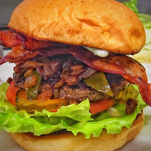 A Bubba's Texas Burger Shack burger with bacon, grilled onions, jalapeños, pickles, tomato, and lettuce.